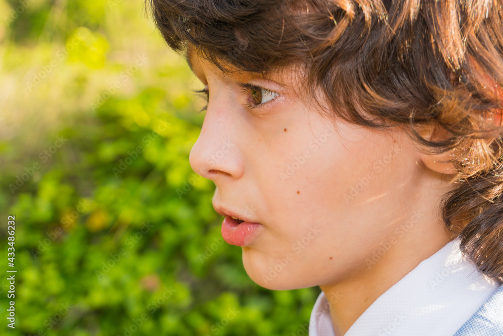 White boy with white shirt, brown hair and a little long, green vegetation and flowers background. White boy with white shirt, brown hair and a little long, green vegetation and flowers background.