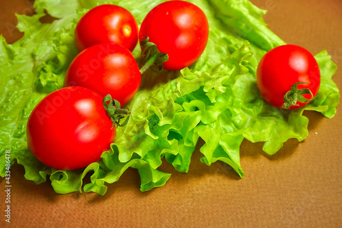 Red cherry tomatoes lie on a lettuce leaf.