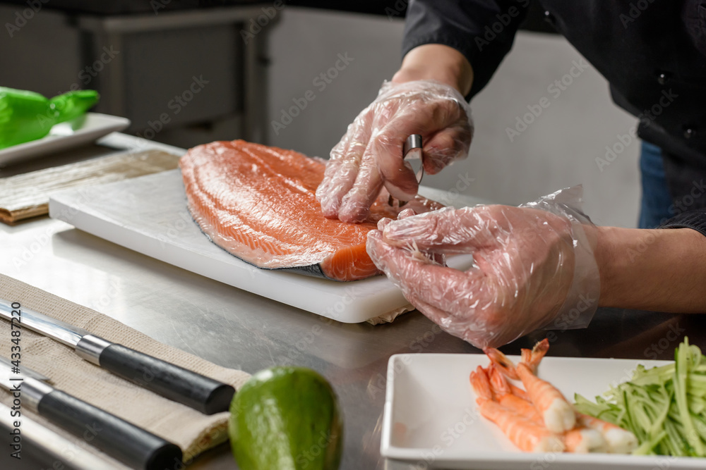 The process of cooking fish dishes. Japanese restaurant cuisine. The sushi chef holds a kitchen fish tweezers in his hand and removes bones from a fresh salmon fillet. Ingredients for sushi rolls.