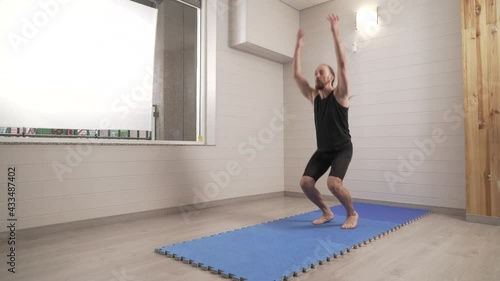 Sporty male training at home. He performs squat jumps with high intensity