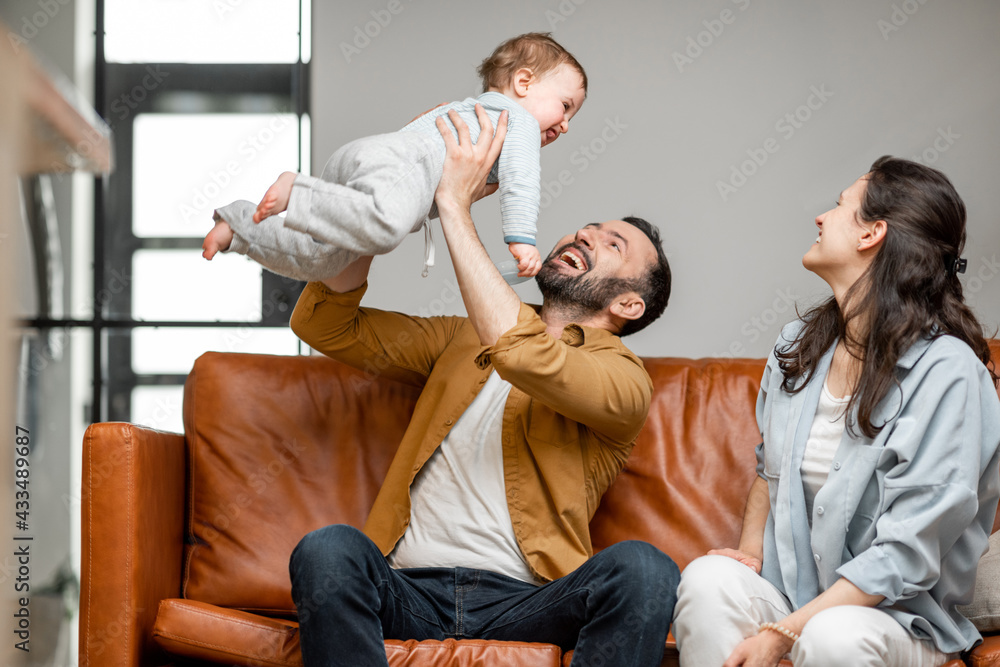 Happy father, mother and little son are playing on sofa in living room. Child care and parenting. Dad throws the baby up. Happy father, mother and little son are playing on sofa in living room. Child care and parenting. Dad throws the baby up.