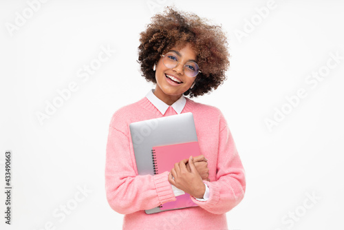 Laughing funny african american teen girl, online course or high school student holding laptop and pink notebook, isolated on gray background