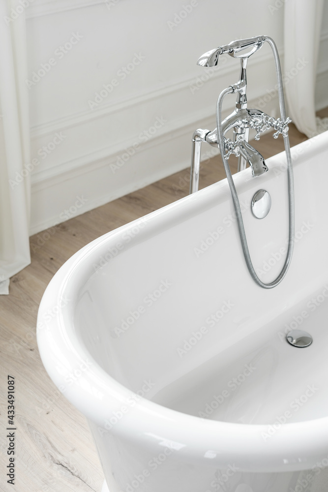 White freestanding bathtub on wooden floor in bathroom White freestanding bathtub on wooden floor in bathroom