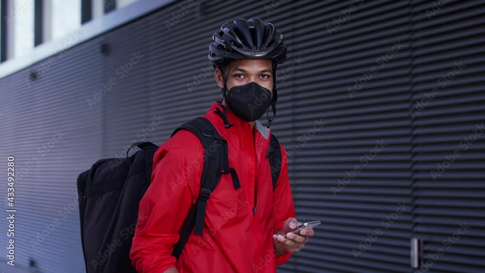 Young courier delivering a food on bike, looking at camera. Coronavirus concept. Young courier delivering a food on bike, looking at camera. Coronavirus concept.
