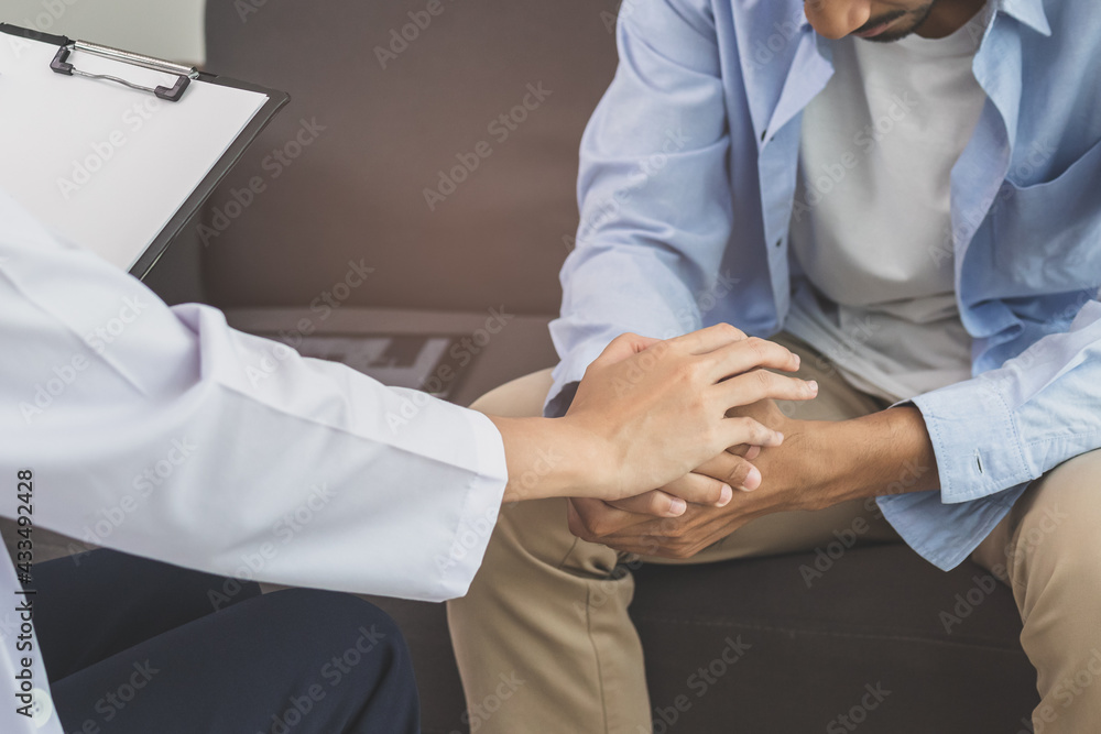 Asian young man, male suffers from a mental who needs to therapy with a psychologist while sitting on couch to consult, psychiatrist has encouragement the patient by touching to make his feel relaxed. Asian young man, male suffers from a mental who needs to therapy with a psychologist while sitting on couch to consult, psychiatrist has encouragement the patient by touching to make his feel relaxed.