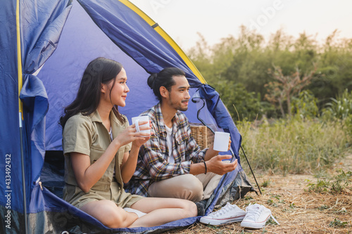 Happy young asian woman, girl and man drinking with mug of coffee, sitting in the tent. Adventure couple, people camping in forest. Eco activity, lifestyle nature on holiday concept.