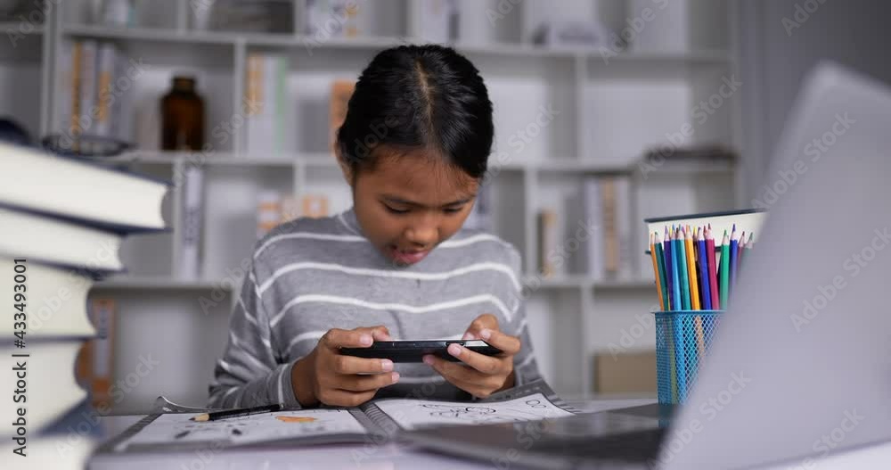Thai girl playing game on mobile phone and lost while studying online at home. Thai girl playing game on mobile phone and lost while studying online at home.