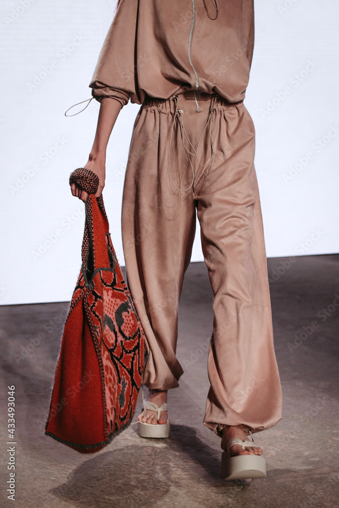 Fototapeta premium Cropped figure of fashion model woman wearing beige trendy sport outfit and stylish red bag. Casual outfit. Vertical shot