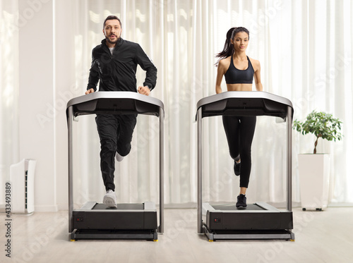 Young man and woman running on treadmills with curtain in the background