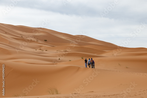 group of people walk along the sand dunes in the Sahara Desert. Morocco