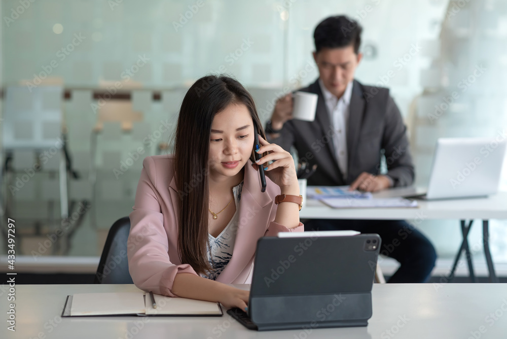 Front view of businesswoman talking on the phone and using tablet notebook placed on the office table the back is blurry. Front view of businesswoman talking on the phone and using tablet notebook placed on the office table the back is blurry.