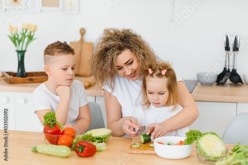Young mother and her two kids making vegetable salad