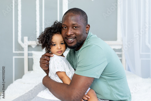 happy African-American dad hugs baby daughter on bed at home, happy family
