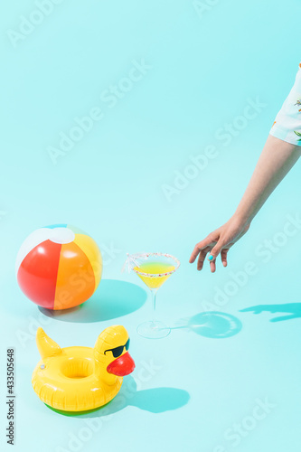 unknown person drinking a cocktail. next to him is a beach ball and an inflatable duck on a blue background.