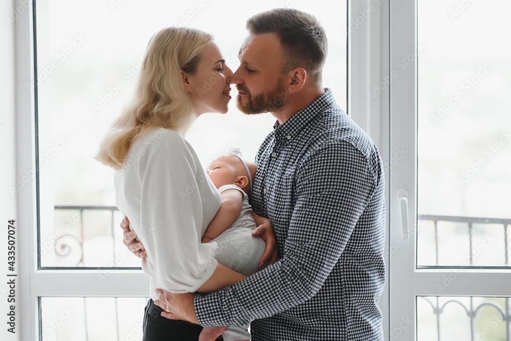View at Happy family with newborn baby by the window View at Happy family with newborn baby by the window