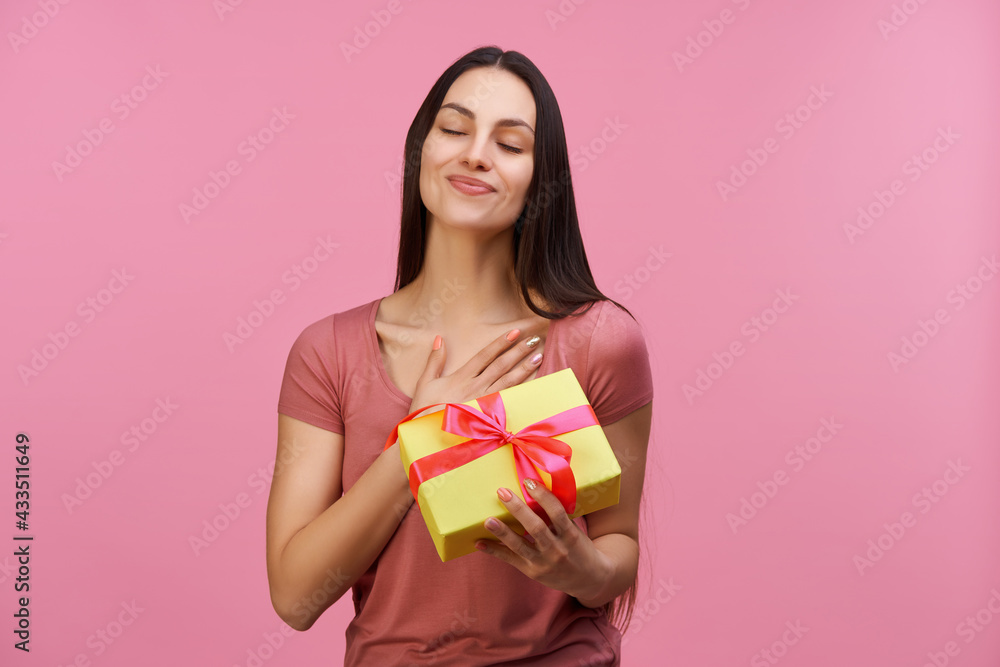 Young casually dressed pretty woman accepting a present with grateful face expression and gesture, isolated over pastel pink background Young casually dressed pretty woman accepting a present with grateful face expression and gesture, isolated over pastel pink background