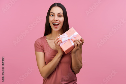 Studio shot of cute joyful brunette girl holding gift box with excited open mouth face expression © wpadington