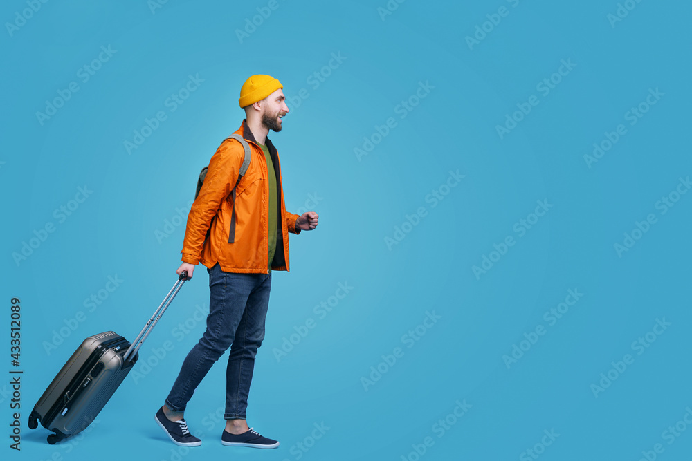 Full-length portrait of casually dressed young bearded man tourist walking in the airport terminal with a backpack and hand luggage bag Full-length portrait of casually dressed young bearded man tourist walking in the airport terminal with a backpack and hand luggage bag
