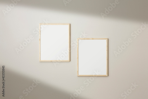 Set of two frames mockup. Thin wood frames hanging on a neutral coloured. Window light creating long shadows.