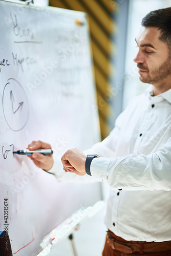 the company manager in a white shirt writes on a flipchart and looks at the watch on his hand. time management. plans and is ready to train staff, conduct lectures and online training.