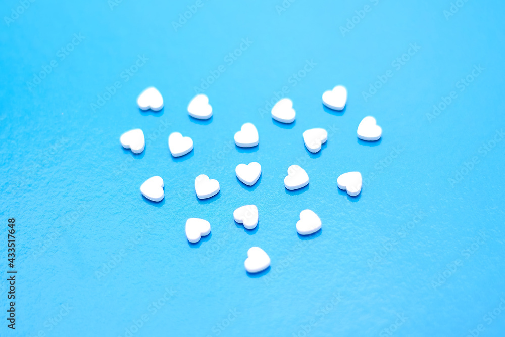 Elevated view of white tablets on blue background. Heart pills. white tablets in the form of small hearts. Medicine pill on a blue background.