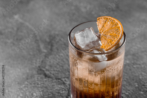 Cocktail in glass with cola, alcohol, ice, decorated dried orange on gray background.