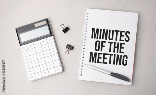 The word MINUTES OF THE MEETING is written on a white background next to a pen ,calculator and reports. Business concept