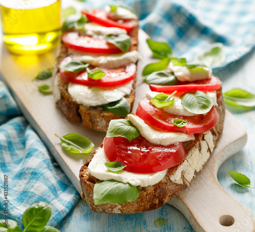 Caprese open faced sandwich based on sourdough bread with the addition of tomatoes, mozzarella cheese, fresh basil and olive oil on a white board close up view