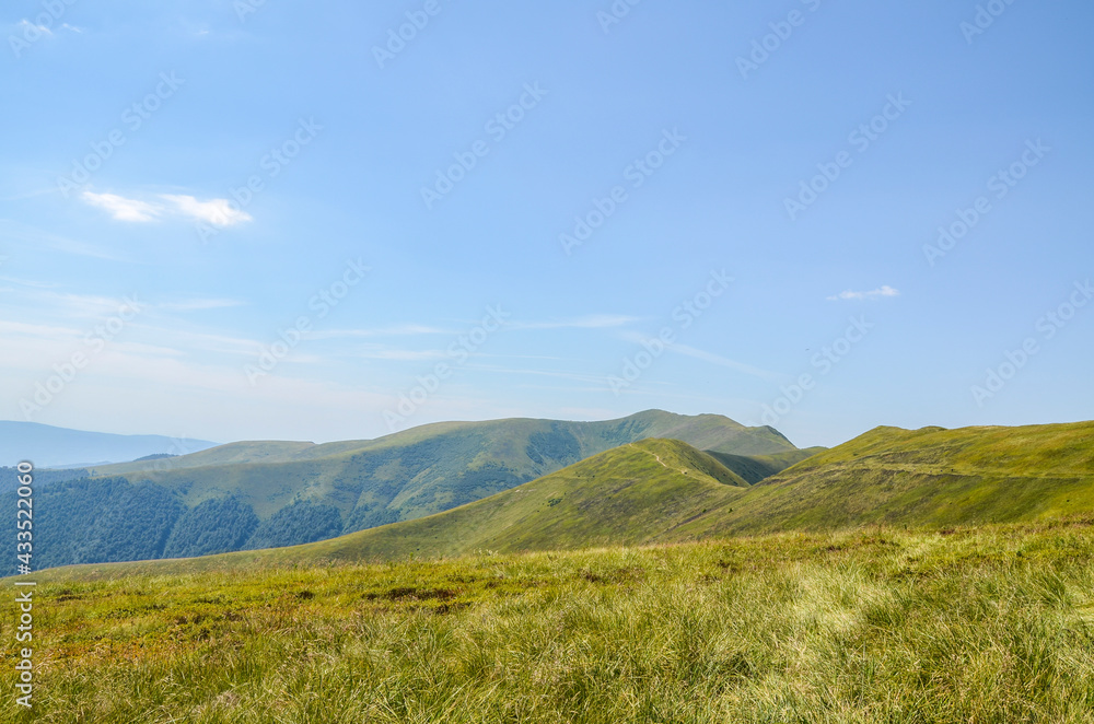 Beautiful summer landscape of Borzhava mountains with green grass on the hillside and blue sky in distance. Path curve beneath high ridge. Carpathians, Ukraine 