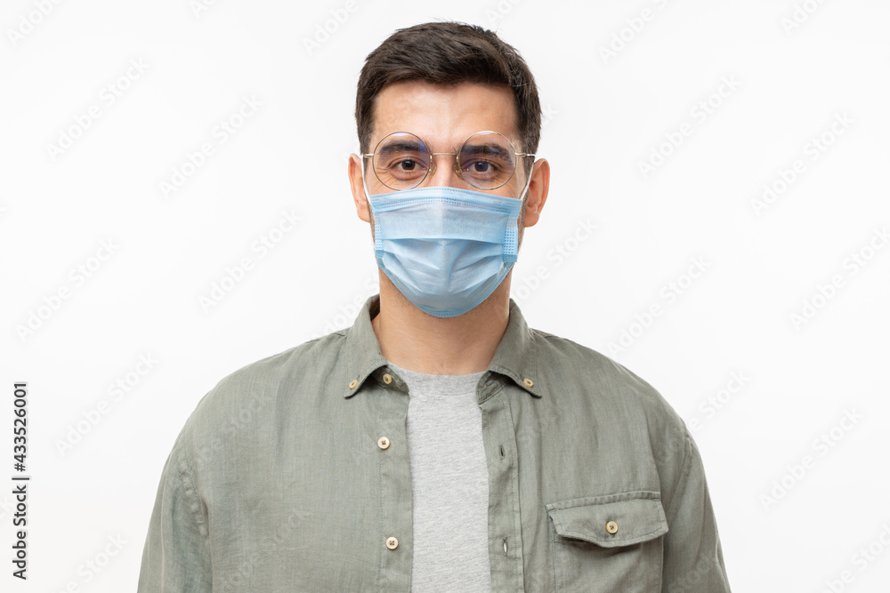 Young modern man wearing shirt and medical mask standing isolated on gray background