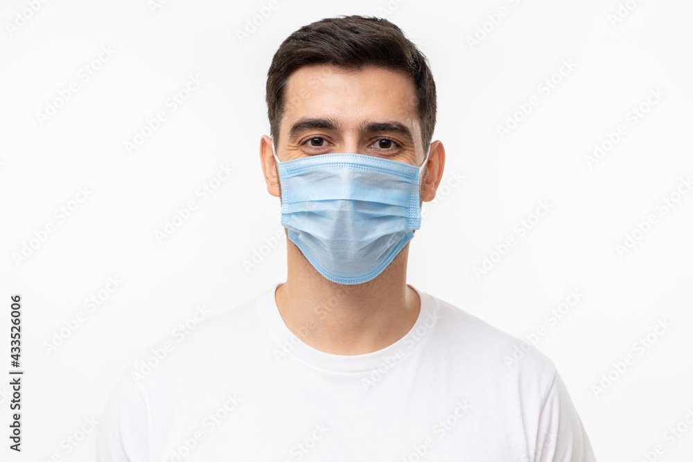 Young handsome man wearing white t-shirt and medical mask, isolated on gray background