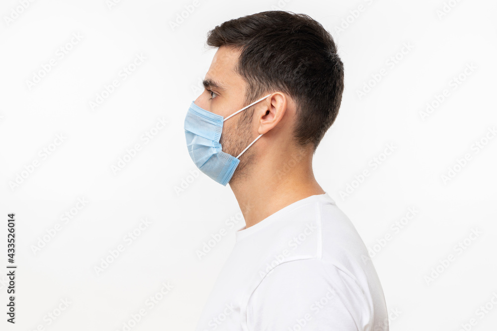 Side view portrait of young man wearing white t-shirt and face mask, isolated on gray background Side view portrait of young man wearing white t-shirt and face mask, isolated on gray background