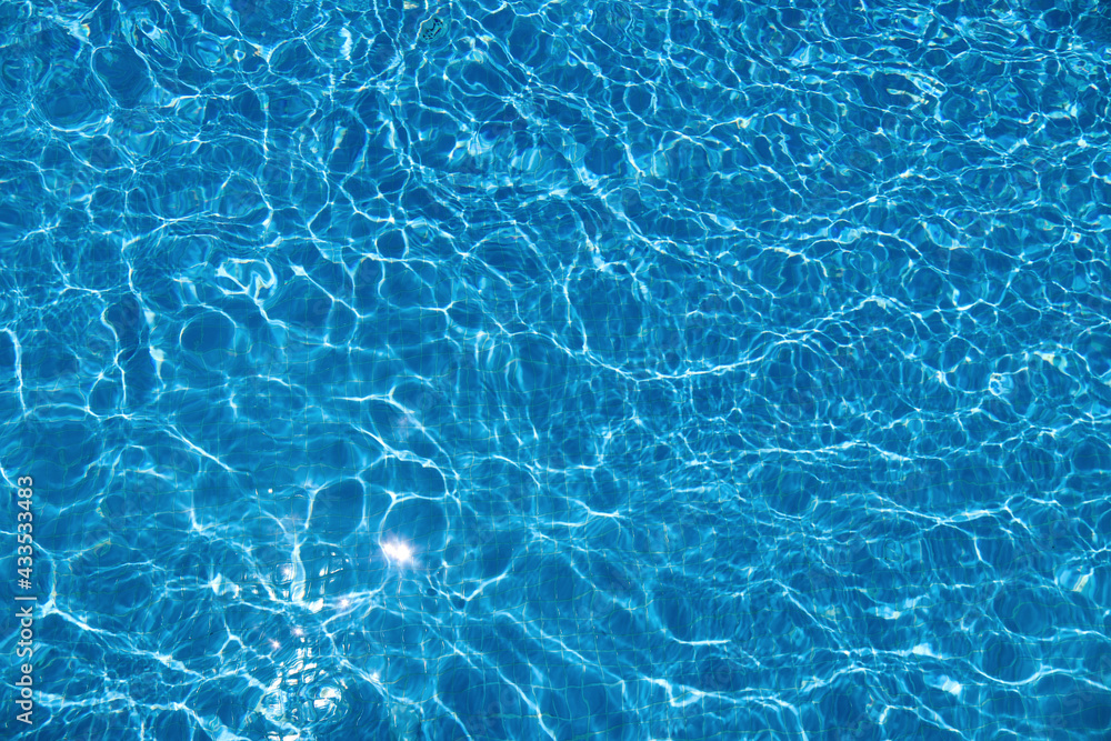 Abstract summer background with clear blue water in the swimming pool and sun reflection. Ripple water and gentle wave