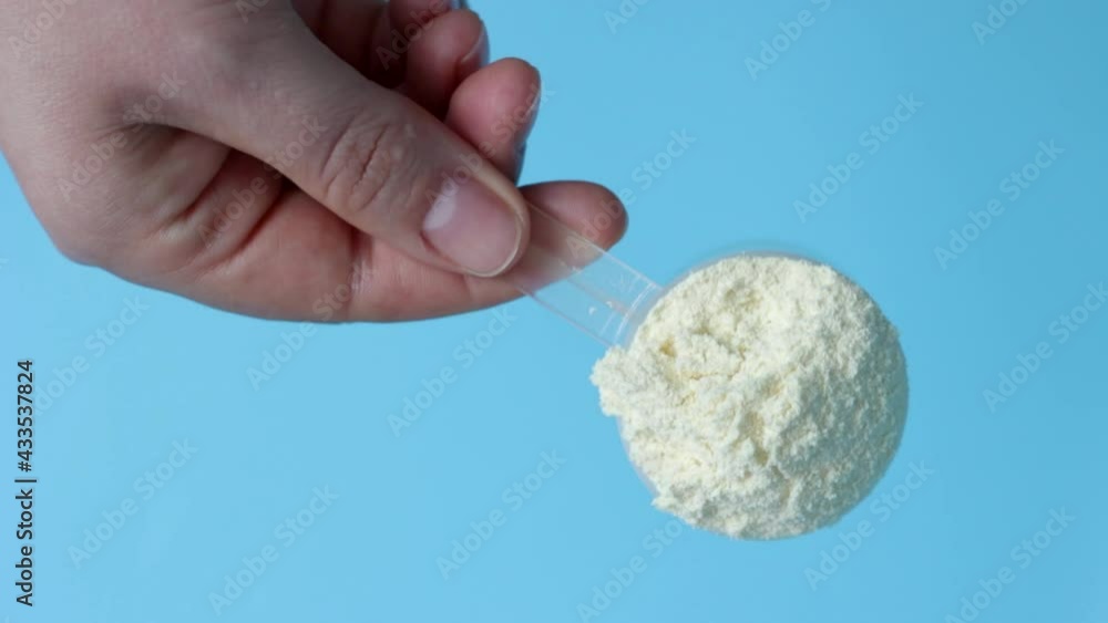 Female hand holding scoop with protein powder on a blue background.