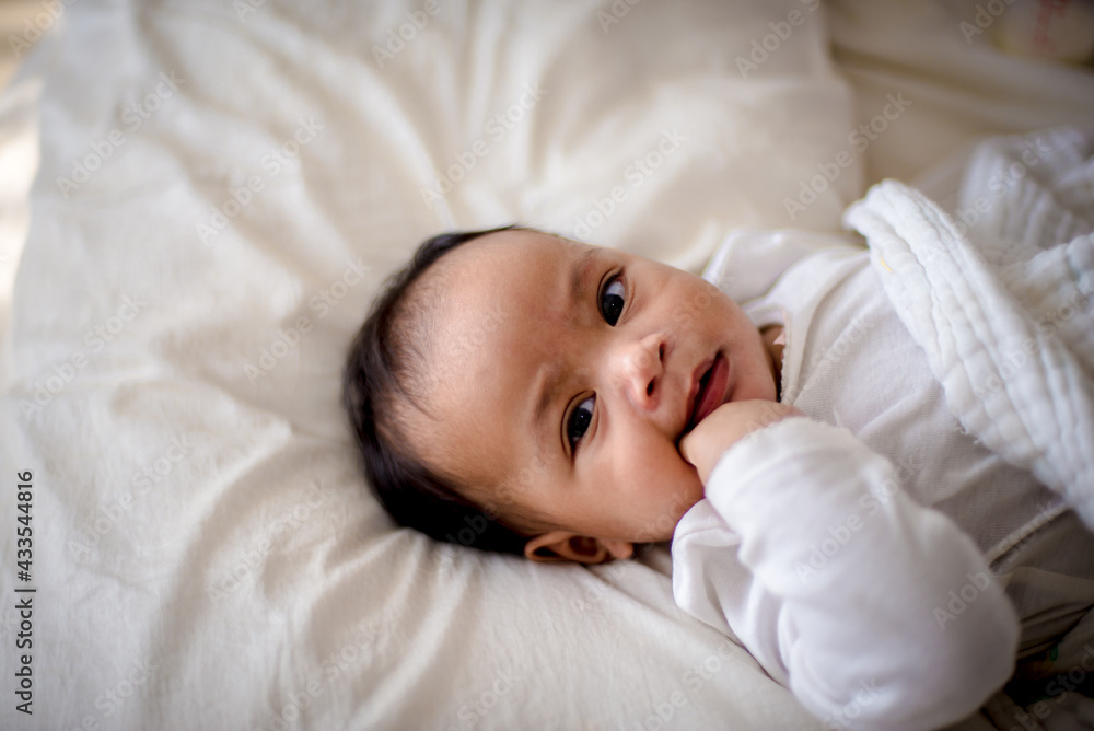 Infants are looking forward in an upside-down position on a white bed, the evolution of Baby girl in the age up to 6 months./Selected focus Infants are looking forward in an upside-down position on a white bed, the evolution of Baby girl in the age up to 6 months./Selected focus