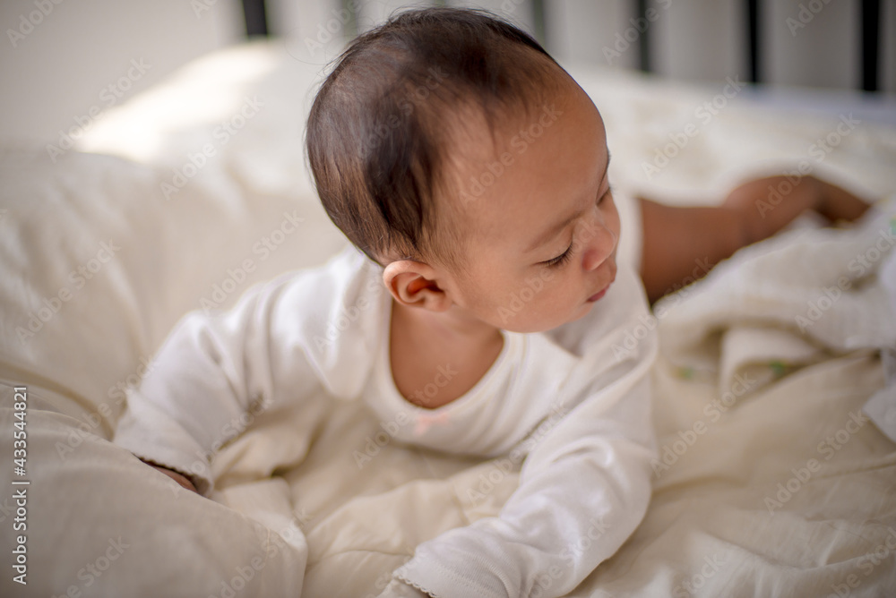 Infants are looking forward in an upside-down position on a white bed, the evolution of Baby girl in the age up to 6 months./Selected focus Infants are looking forward in an upside-down position on a white bed, the evolution of Baby girl in the age up to 6 months./Selected focus