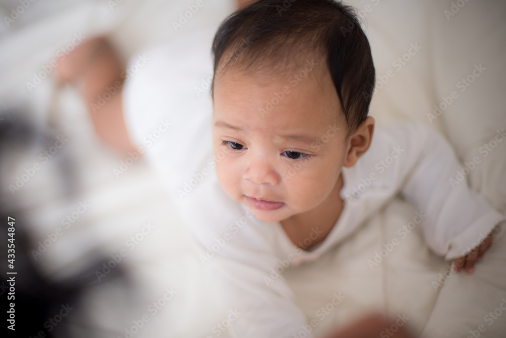 Infants are looking forward in an upside-down position on a white bed, the evolution of Baby girl in the age up to 6 months./Selected focus Infants are looking forward in an upside-down position on a white bed, the evolution of Baby girl in the age up to 6 months./Selected focus