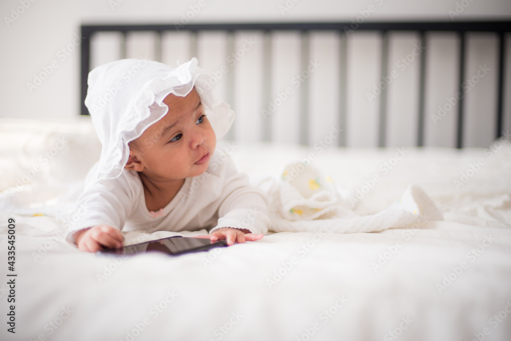 Infants are looking forward in an upside-down position on a white bed, the evolution of Baby girl in the age up to 6 months./Selected focus Infants are looking forward in an upside-down position on a white bed, the evolution of Baby girl in the age up to 6 months./Selected focus