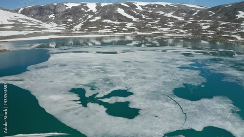 Almost free of the grip of winter. Ice is floating in the turquoise waters of the mountain lake in the Strynfjellet mountains. Patches of snow laying on the mountainsides Sun is bright in the blue sky photo