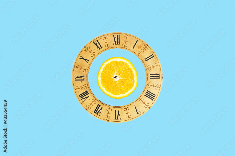 Simple concept with a slice orange and a vintage clock dial on blue background