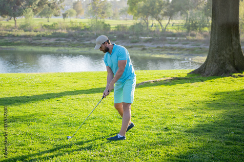 Golf club, man is standing on the green grass of the lawn on a golf field on a warm evening.