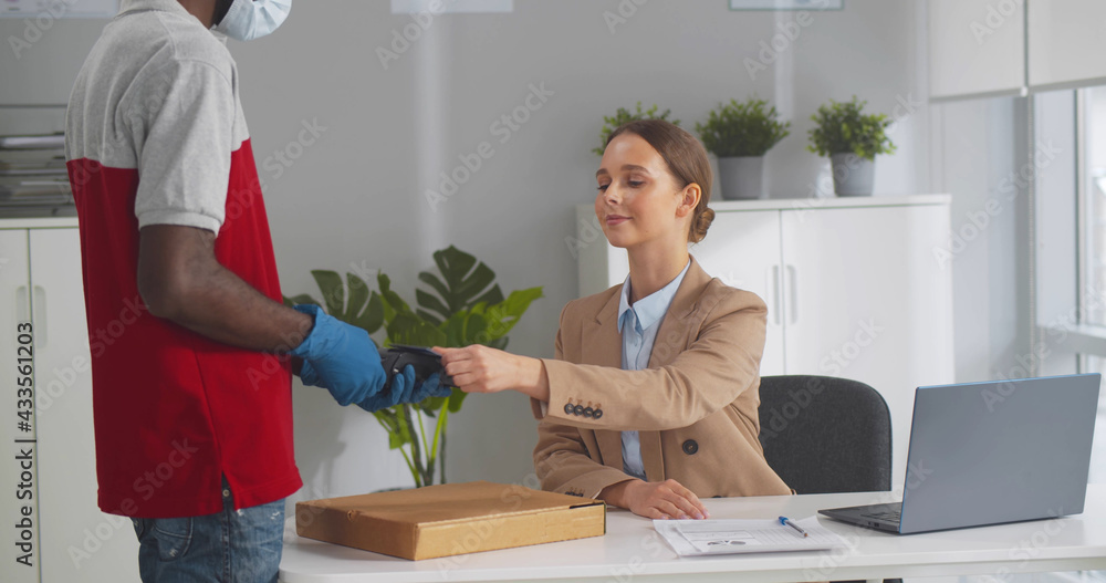 Obraz premium Deliveryman in mask and gloves giving pizza box to female office worker paying with credit card