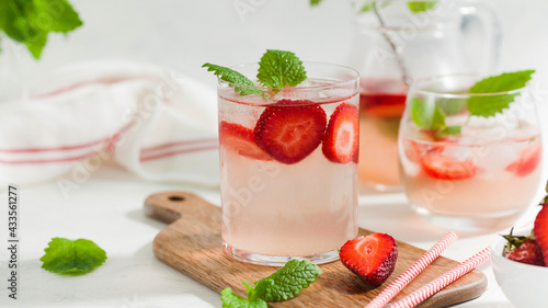 Homemade refreshing strawberry lemonade in pitcher and glass on a wooden board
