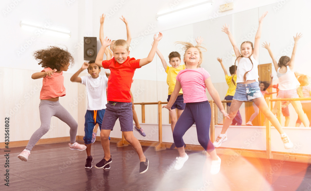 Group of happy sporty kids with female teacher training in modern dance studio, jumping together