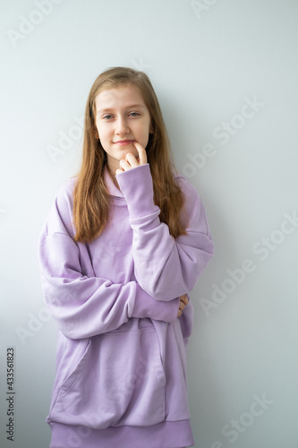 teenage girl with long hair in purple huddy standing against white wall looking at camera photo