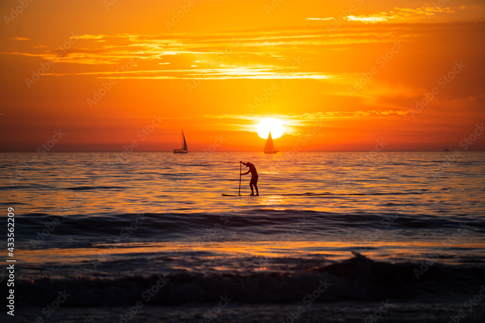 Sunset silhouette of paddle board on a sea. Relaxing on ocean. Sunrise over the sea and beautiful cloudscape. Colorful ocean beach sunset. Seascape golden sunrise over the sea.