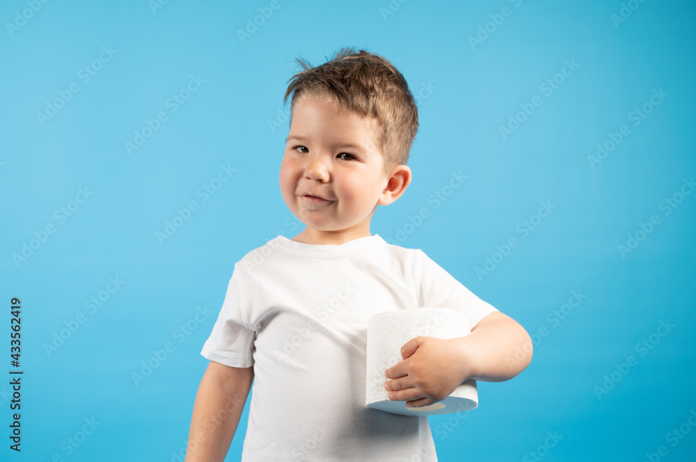 A little boy gently holds in his hand roll of toilet paper on blue background. The buying toilet paper concept A little boy gently holds in his hand roll of toilet paper on blue background. The buying toilet paper concept