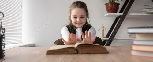 A cheerful little schoolgirl sits at the table and pushes the textbook aside with her hands. Friday, the end of the working day. Baner.