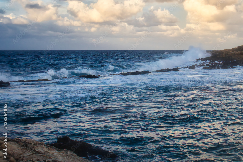 Water crashing over a line of rocks in the ocean at Qawra, Malta on a fall evening.