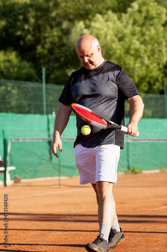An adult man plays tennis on a street court on a sunny day. Sports and active lifestyle. Vertical. © Анна Демидова